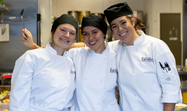 3 escoffier culinary students embrace for a photo in the kitchen